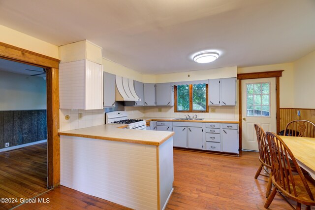 kitchen featuring light wood-type flooring, exhaust hood, kitchen peninsula, gas range gas stove, and sink