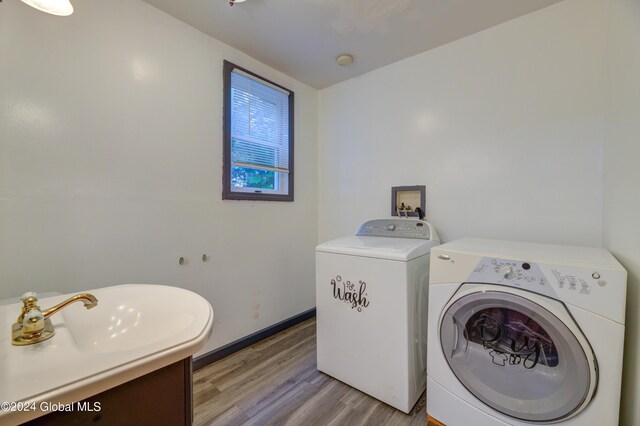 laundry room featuring washing machine and dryer, sink, and light wood-type flooring