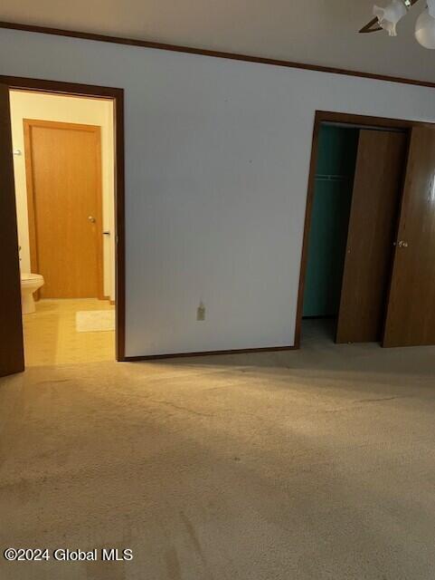 unfurnished bedroom featuring light carpet, a closet, crown molding, ensuite bath, and ceiling fan