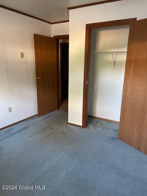 unfurnished bedroom with a closet, carpet flooring, and crown molding