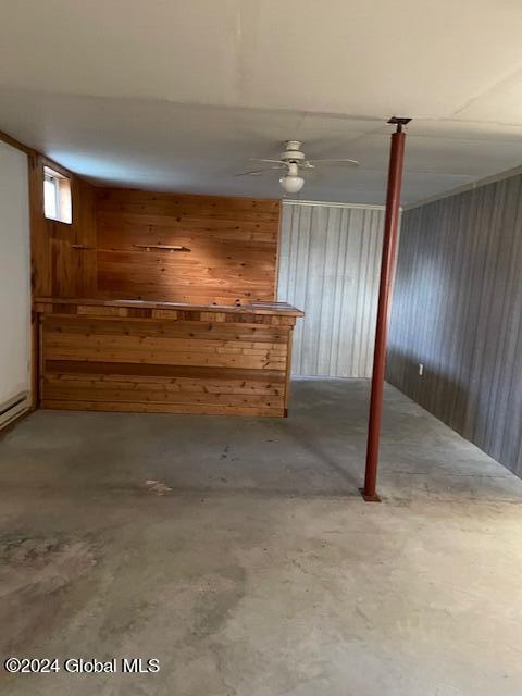 basement featuring ceiling fan and wooden walls