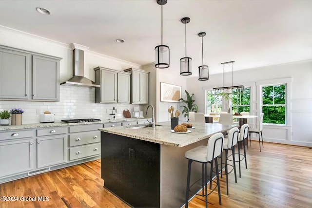 kitchen featuring a center island with sink, pendant lighting, sink, and wall chimney range hood