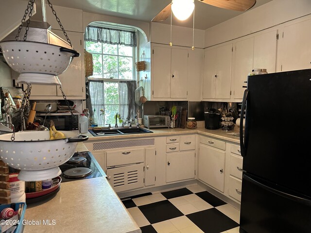 kitchen featuring ceiling fan, sink, black fridge, and white cabinetry