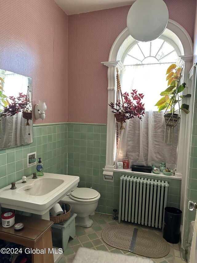 bathroom with tile walls, toilet, radiator heating unit, and tile patterned floors