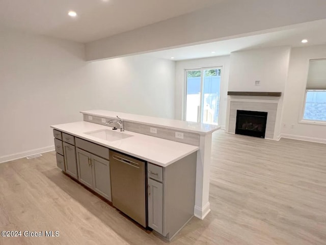 kitchen featuring a kitchen island with sink, plenty of natural light, light hardwood / wood-style flooring, and stainless steel dishwasher