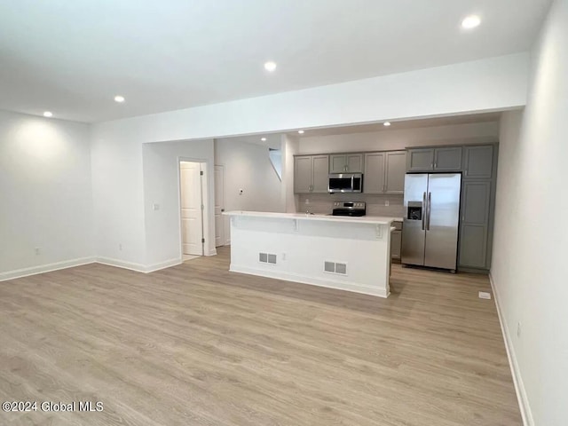 kitchen with gray cabinets, light wood-type flooring, stainless steel appliances, and a center island with sink