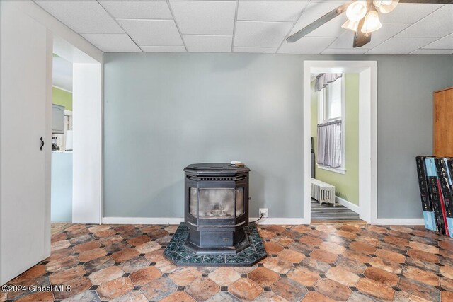 interior details featuring a wood stove, ceiling fan, a paneled ceiling, and radiator