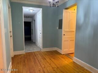 hall featuring wood-type flooring, crown molding, and a notable chandelier