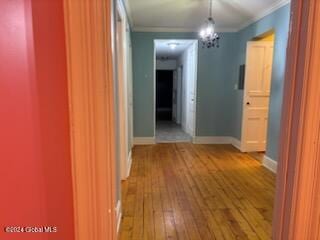 corridor featuring wood-type flooring, ornamental molding, and a chandelier