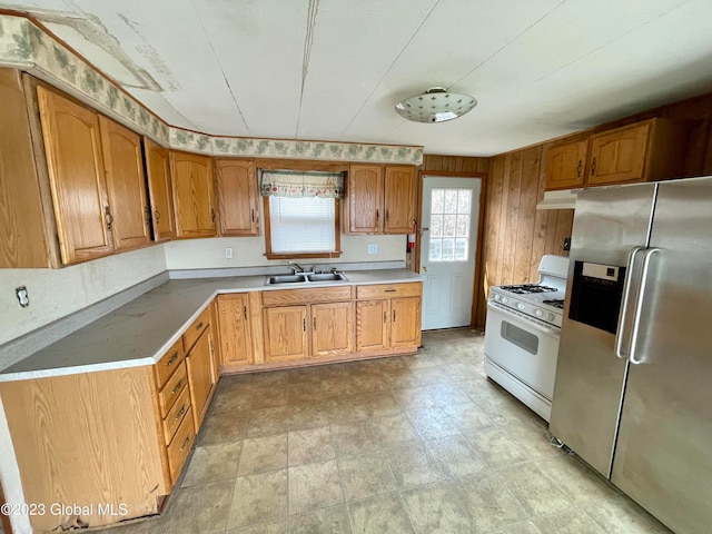 kitchen featuring stainless steel refrigerator with ice dispenser, wood walls, gas range gas stove, and sink