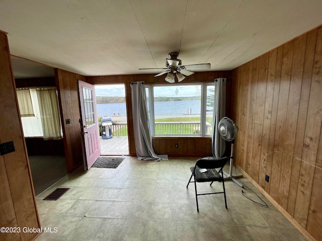 interior space featuring a water view, ceiling fan, wooden walls, and a healthy amount of sunlight