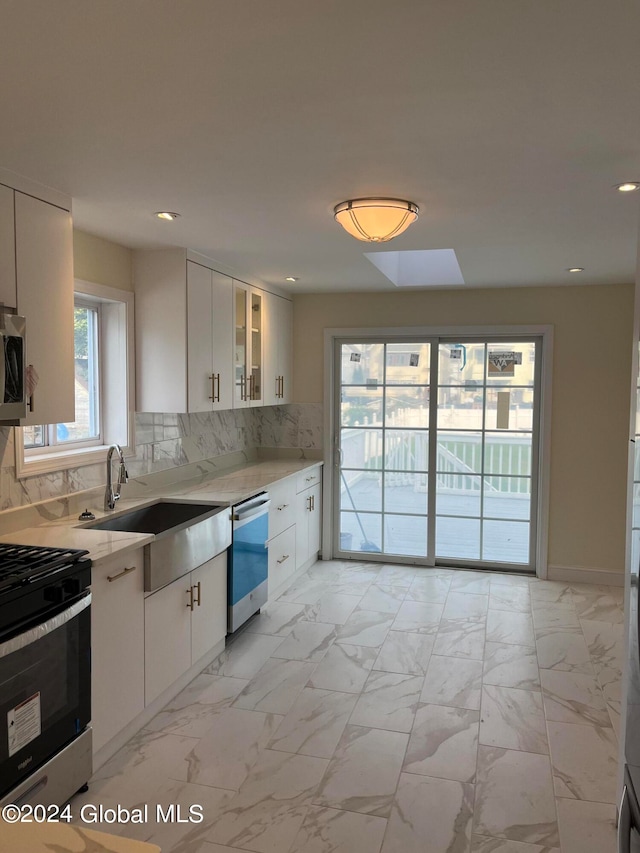 kitchen with white cabinets, a skylight, sink, stainless steel appliances, and decorative backsplash