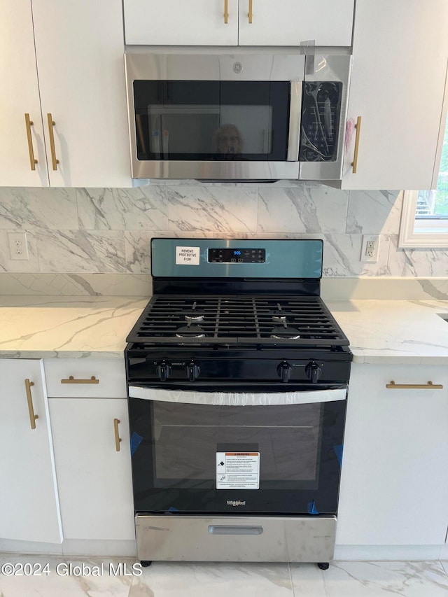 kitchen featuring light stone countertops, stainless steel appliances, backsplash, and white cabinetry