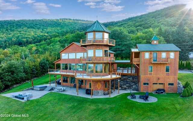 back of house with a garage, a balcony, a patio, a fire pit, and a lawn