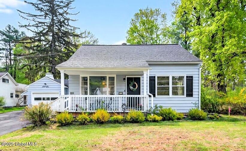 bungalow-style home featuring a porch, an outdoor structure, a garage, a front lawn, and driveway