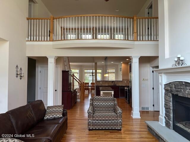 living room with a fireplace, wood-type flooring, ornate columns, and a high ceiling