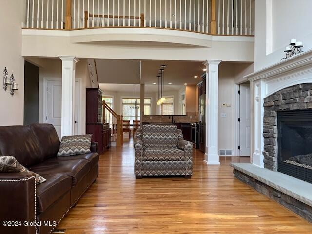 living room featuring light hardwood / wood-style flooring, decorative columns, and a stone fireplace