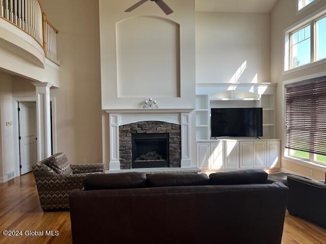 living room featuring a healthy amount of sunlight, ceiling fan, a stone fireplace, and light wood-type flooring