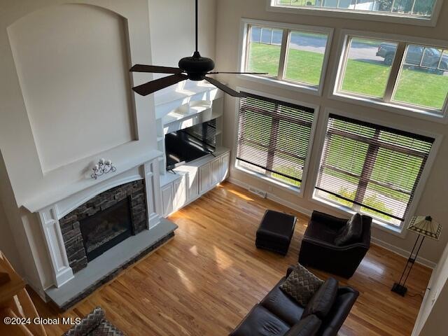 living room featuring light hardwood / wood-style floors, a healthy amount of sunlight, ceiling fan, and a stone fireplace