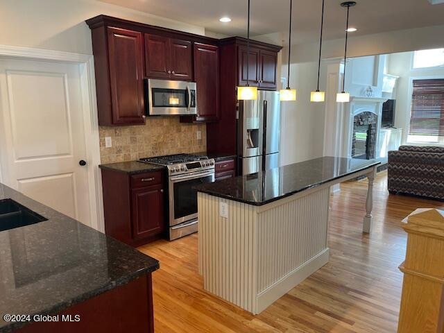 kitchen with light wood-type flooring, dark stone counters, tasteful backsplash, stainless steel appliances, and hanging light fixtures