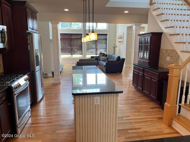 kitchen with appliances with stainless steel finishes, light hardwood / wood-style flooring, ornate columns, and a notable chandelier