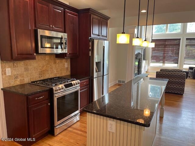 kitchen with a center island, backsplash, light wood-type flooring, and appliances with stainless steel finishes