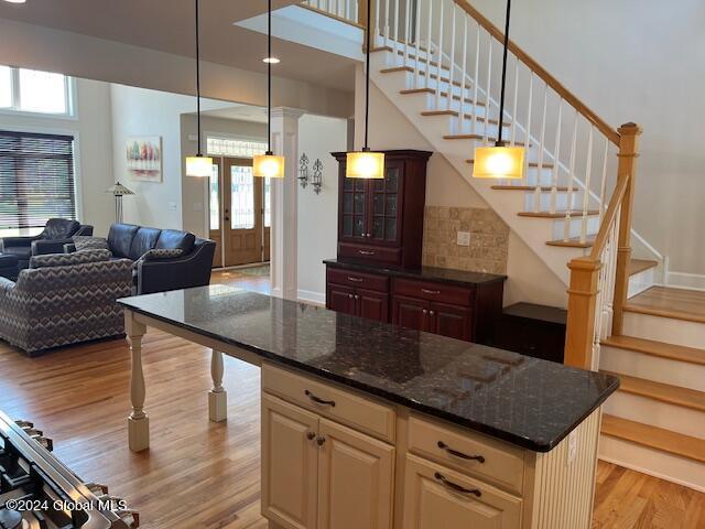 kitchen with dark stone counters, decorative light fixtures, cream cabinetry, and light hardwood / wood-style floors