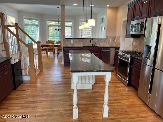 kitchen with decorative light fixtures, appliances with stainless steel finishes, light hardwood / wood-style floors, a notable chandelier, and sink