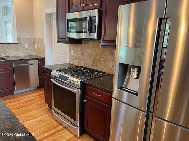 kitchen featuring light hardwood / wood-style flooring, stainless steel appliances, dark stone countertops, and decorative backsplash