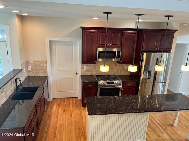 kitchen featuring light wood-type flooring, appliances with stainless steel finishes, sink, and hanging light fixtures