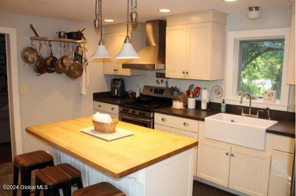 kitchen with stainless steel stove, premium range hood, sink, and white cabinetry