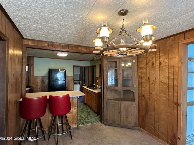 kitchen featuring dark carpet, wooden walls, black refrigerator, and sink