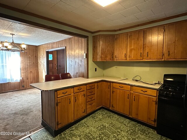 kitchen with carpet floors, kitchen peninsula, black range with gas cooktop, wooden walls, and a chandelier