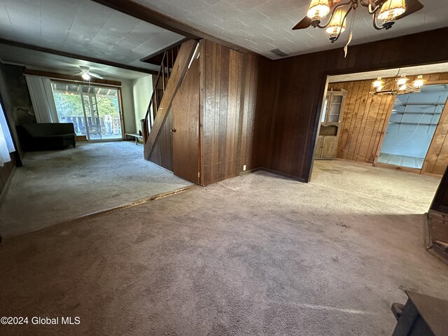 unfurnished living room featuring ceiling fan with notable chandelier, wooden walls, and carpet