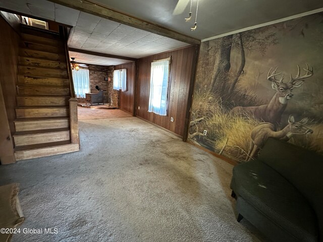 unfurnished living room with a wood stove, carpet, ceiling fan, and wooden walls