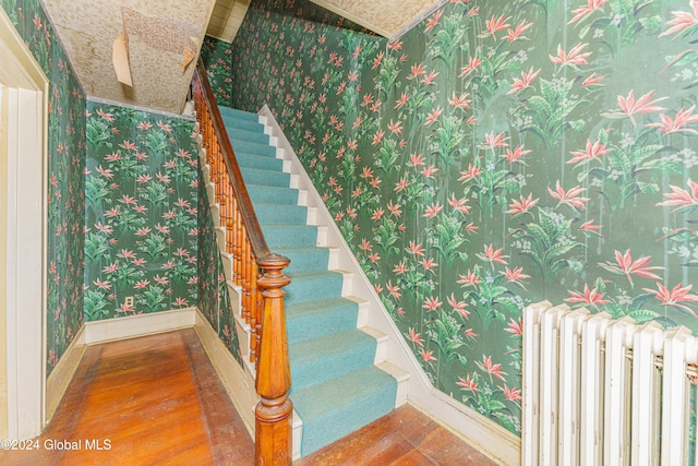 staircase with hardwood / wood-style floors and radiator heating unit