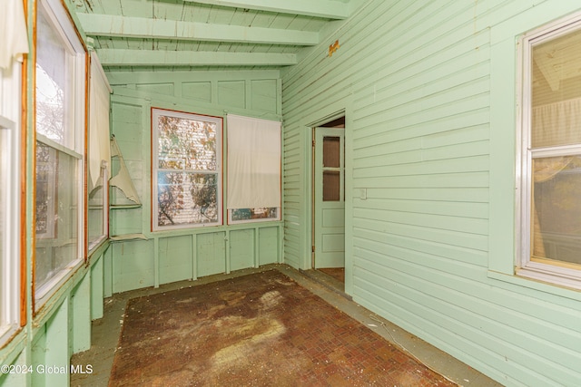 unfurnished sunroom featuring lofted ceiling with beams and a wealth of natural light