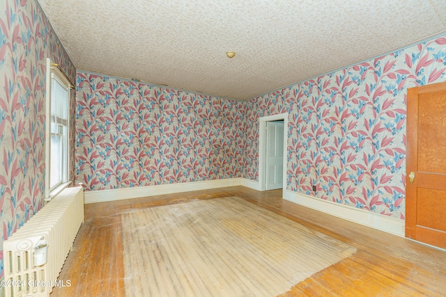 unfurnished room featuring radiator heating unit and hardwood / wood-style flooring