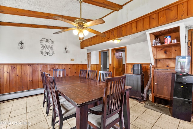 tiled dining space with ceiling fan, wood walls, a textured ceiling, lofted ceiling with beams, and a baseboard radiator