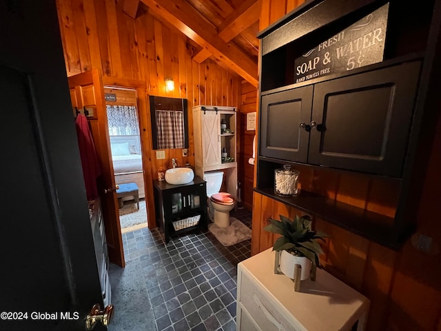 bathroom with wood walls, tile patterned flooring, toilet, vaulted ceiling with beams, and sink