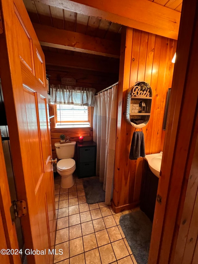 bathroom featuring wood walls, beamed ceiling, tile patterned floors, and toilet