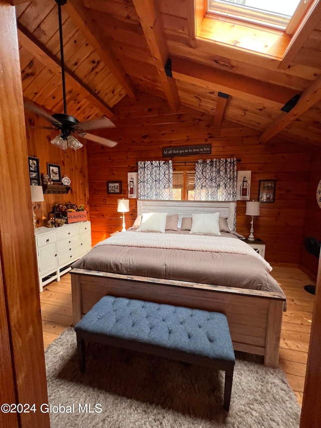 bedroom featuring ceiling fan, vaulted ceiling with skylight, wood ceiling, wooden walls, and light hardwood / wood-style floors