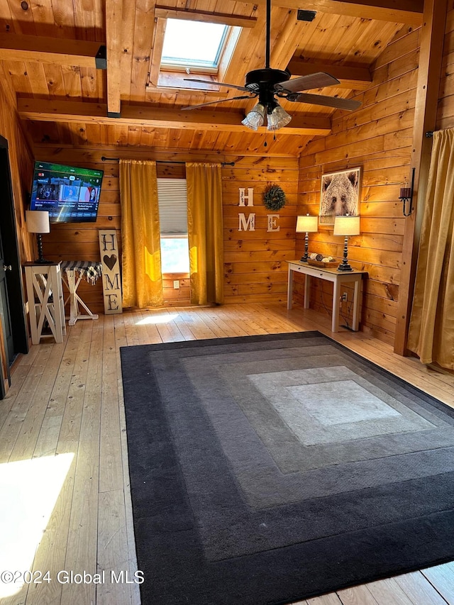 interior space with ceiling fan, wood walls, lofted ceiling with skylight, wooden ceiling, and hardwood / wood-style floors