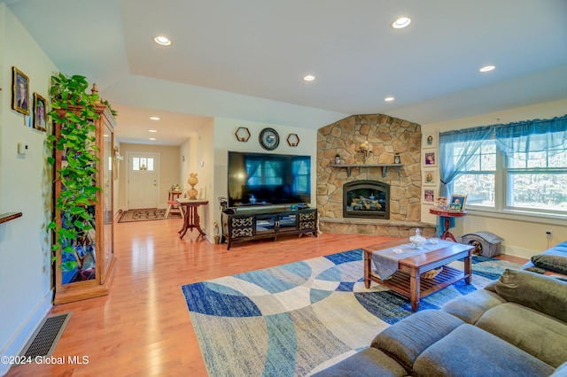 living room featuring vaulted ceiling, light wood-type flooring, and a stone fireplace