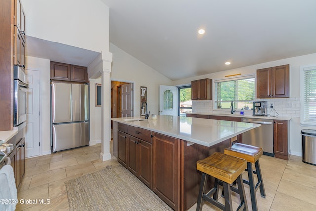 kitchen featuring appliances with stainless steel finishes, a center island with sink, a breakfast bar, and ornate columns