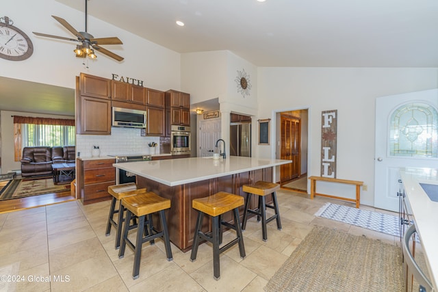 kitchen featuring appliances with stainless steel finishes, an island with sink, high vaulted ceiling, a kitchen bar, and ceiling fan