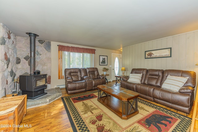 living room with a baseboard heating unit, hardwood / wood-style flooring, wooden walls, and a wood stove