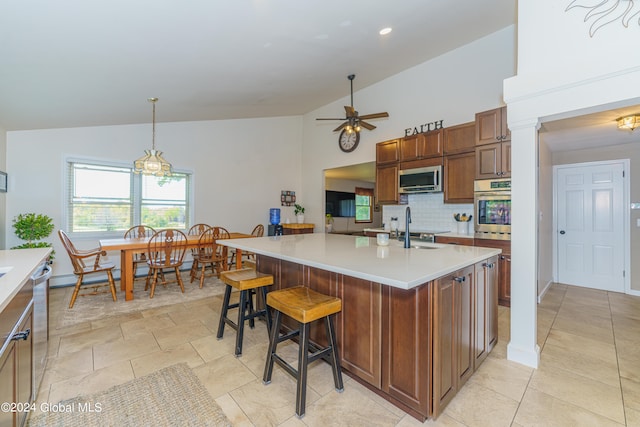 kitchen featuring ceiling fan, hanging light fixtures, a center island with sink, backsplash, and appliances with stainless steel finishes