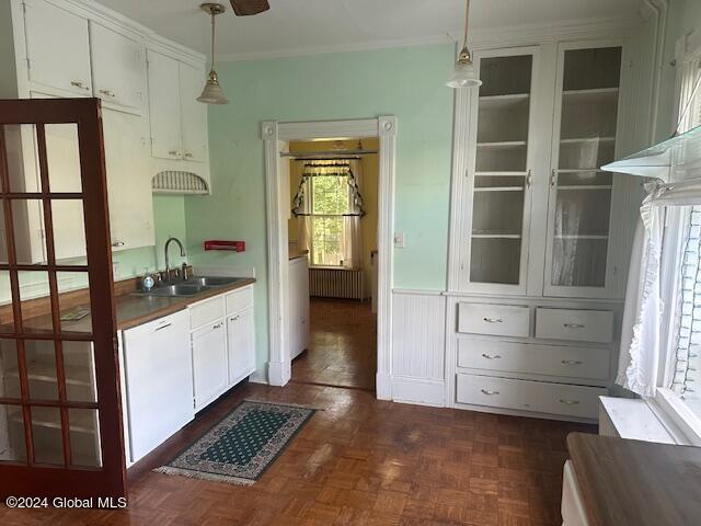 kitchen with dark parquet flooring, white cabinets, crown molding, decorative light fixtures, and sink