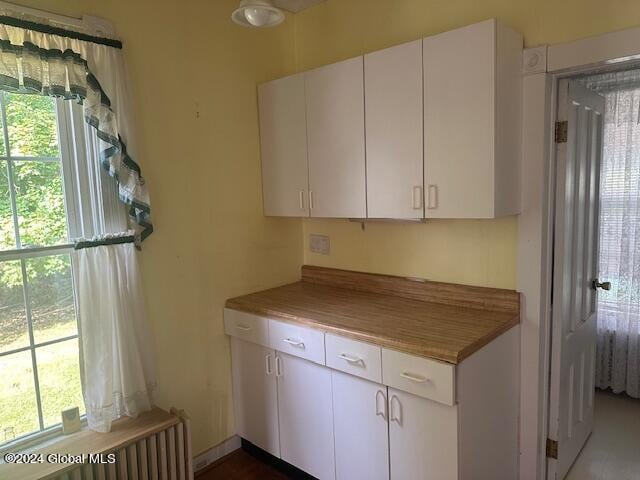 kitchen featuring a wealth of natural light, radiator heating unit, and white cabinetry